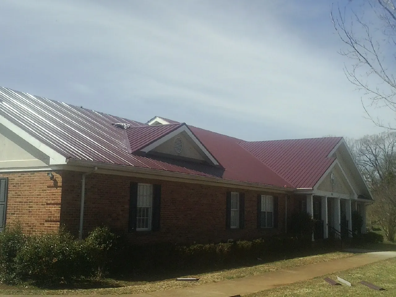Red metal roof with gabled entries on a long brick building, from a Hail Damage Roof Repair job in Dundee