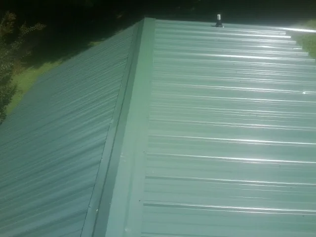 New green metal panels meeting at the ridge of a roof — Flat Roof Repair work by our crew in Dundee